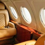 Interior Cabin Of A Private Jet With Tan Leather Seats And A Wood Trimmed Table
