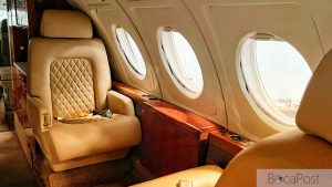 Interior Cabin Of A Private Jet With Tan Leather Seats And A Wood Trimmed Table